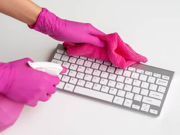 Person cleans laptop keyboard with isopropyl alcohol and microfiber cloth.

