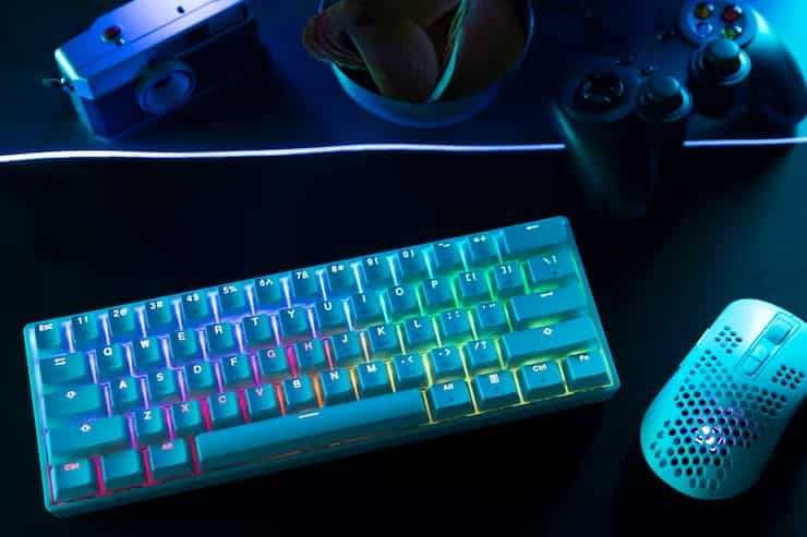 Image of a mechanical keyboard sitting on a desk next to a mouse. The keyboard is black with blue keycaps and has a white LED backlight. 