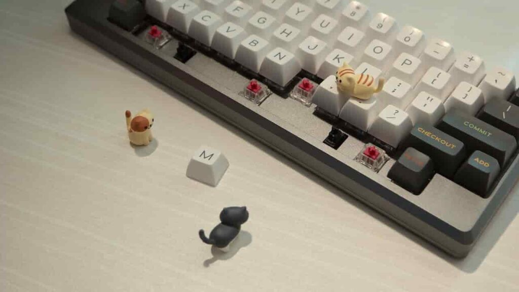 A keyboard with keycaps falling off is adorned by a small toy cat and dog, adding a touch of whimsy to the disarray.